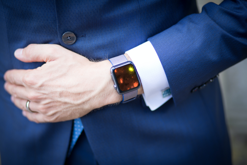 person in a blue suit with one arm extended over the stomach exposing an Apple watch with a photo of cremated remains as stars on the background