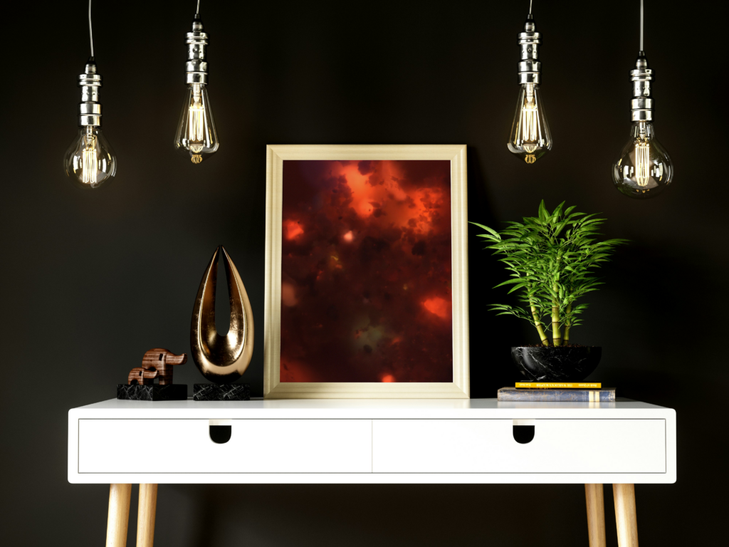 cremation photography peice of art framed in a gold frame on a white table with a small bamboo tree to the right and a trophy in stone elephant to the left with four exposed lightbulbs hanging above framed art